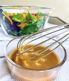 a bowl filled with dressing next to a glass bowl full of salad and a whisk