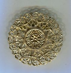 an intricately designed gold brooch sits on a white surface