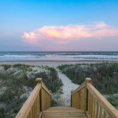 the stairs lead down to the beach at sunset with pink clouds in the sky above