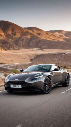 a silver sports car driving down the road in front of mountains and hills at sunset