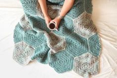 a woman laying on top of a bed covered in a blanket and holding a cup