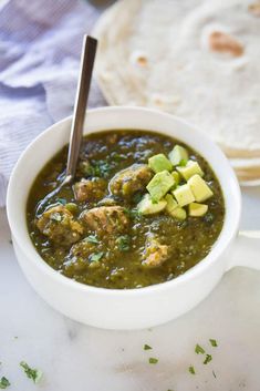 a white bowl filled with meat and vegetable soup next to some bread on the side