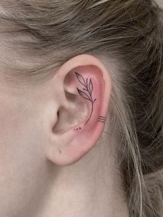 a woman's ear with a small leaf tattoo on it