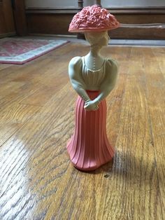 a small figurine wearing a pink dress and hat sitting on a wooden floor