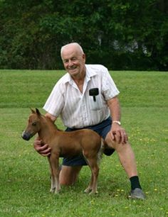 an older man kneeling down next to a small horse