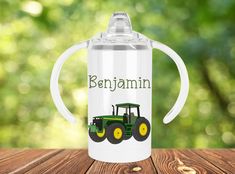 a personalized sippy cup with a tractor on the front and name in green