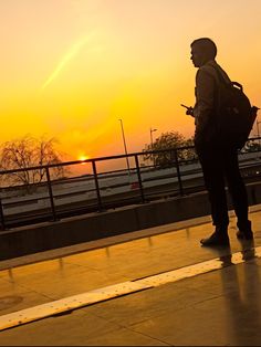 a man is standing on the sidewalk with his back to the camera as the sun sets