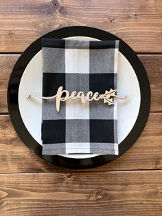 a black and white plate with a plaid napkin that says peace on it, sitting on a wooden table