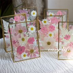 three frames with flowers in them sitting on a white tablecloth and one has a pink flower inside