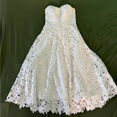 a white dress is laying on a green sheet and it's made out of lace