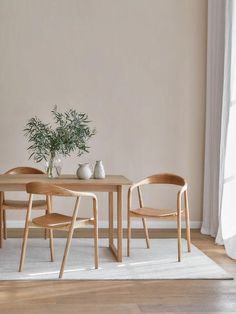 two wooden chairs and a table in front of a white wall with a potted plant on it