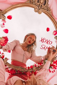 a woman in a pink dress looking at herself in a mirror with roses on it