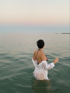 a woman sitting in the water with her back turned to the camera and arms outstretched