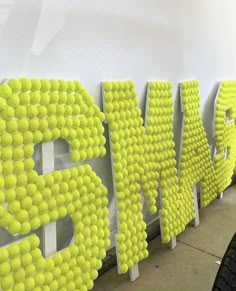 the letters are made out of tennis balls and placed on white poles in front of a wall