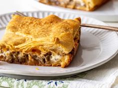 a piece of meat and cheese pie on a plate with a fork next to it