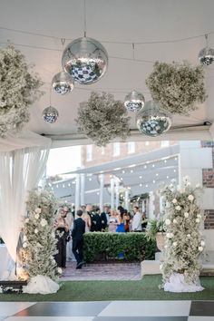 an outdoor ceremony with white flowers and greenery on the ceiling, hanging disco ball chandeliers