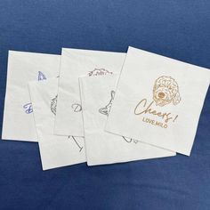 four paper napkins with designs on them sitting on a blue tablecloth covered in writing