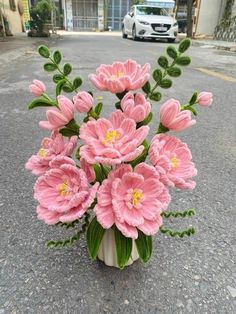 a vase filled with pink flowers sitting on the side of a road