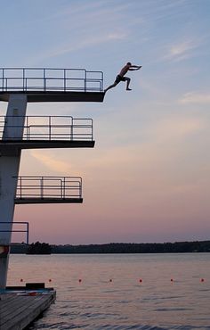 a person jumping into the water from a boat dock at sunset or dawn with no one on it