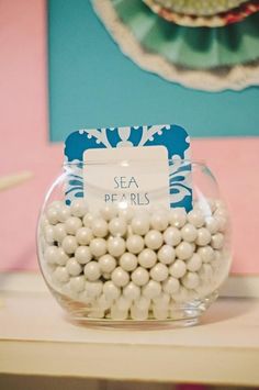 a glass bowl filled with white pearls on top of a wooden table next to a blue and pink wall