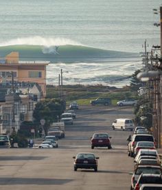 cars are parked on the street in front of an ocean with a wave coming in