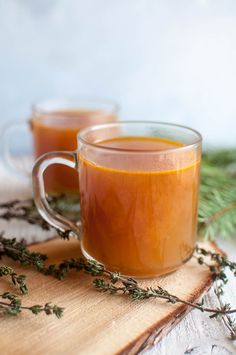 two mugs filled with liquid sitting on top of a cutting board next to some plants