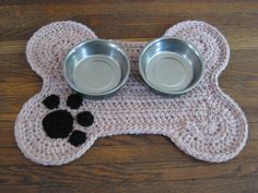 two metal bowls on top of a dog bone shaped place mat with paw prints in the middle