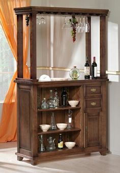 a wooden bar with wine glasses and bottles on the top, in front of a window