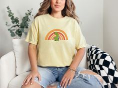 "Cute Dinosaur standing in front of a boho rainbow. Simple and sweet comfy tee. For the oversized look - size up - see size chart for guidance. The photos above show relaxed fit as well as more true to size. Whether you're heading out on a road-trip or hanging out with friends, you'll love the comfortable, oversized fit of this Comfort Colors shirt. The mineral wash feel is super soft and perfect for any casual occasion. Super cute with your favorite jeans, leggings, or just about anything -  you can't go wrong with this super flexible fit -  This is a standard unisex size Comfort Colors Tee.  For an oversized tee, please size up. If you are looking for an oversized \"T-shirt Dress\" look, we recommend sizing up 2 sizes. Please review the size chart to ensure you receive the fit you want." Dinosaur Print Short Sleeve Tops For Spring, Cute Dinosaur Print Top For Spring, Cute Dinosaur Print Tops For Spring, Cute Dinosaur Print Spring Top, Short Sleeve Dinosaur Print Tops For Spring, Cute Spring Dinosaur Print Top, Short Sleeve Tops With Dinosaur Print For Spring, Spring Short Sleeve Tops With Dinosaur Print, Green Dinosaur Print Tops For Spring