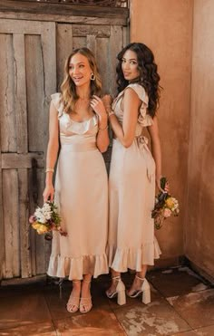 two beautiful women standing next to each other in front of a wooden door holding bouquets