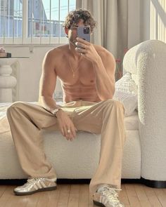 a shirtless man sitting on a couch taking a selfie with his cell phone