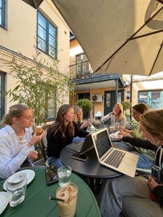 several people sitting at an outdoor table with laptops and drinks in front of them