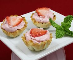 three small pastries with strawberries and mint on a white plate next to a green leaf