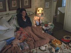 a woman sitting on a bed in a bedroom next to a table with food and drinks