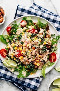 a salad with chicken, tomatoes, corn and lettuce on a white plate