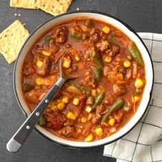 a white bowl filled with chili and corn next to crackers on a black surface