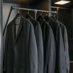 three suits hanging on a rail in front of a mirror with lights above them,