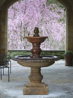 an outdoor fountain in the middle of a patio with pink flowers on trees behind it