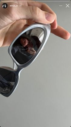 a hand holding up a pair of sunglasses with the reflection of a person in it