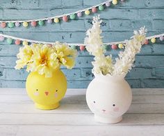 two small vases with flowers in them on a table next to a brick wall