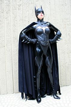 a woman dressed as batman standing in front of a wall with her hands on her hips