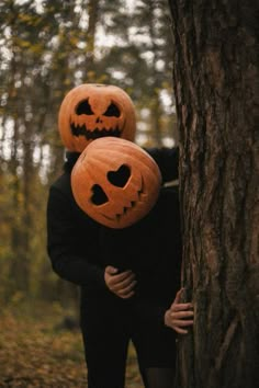 two people with pumpkin heads hugging each other in front of a tree and leaves on the ground