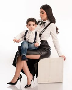 a woman sitting on top of a stool next to a little boy wearing suspenders