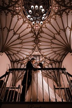 a bride and groom standing on top of a balcony next to an ornate chandelier