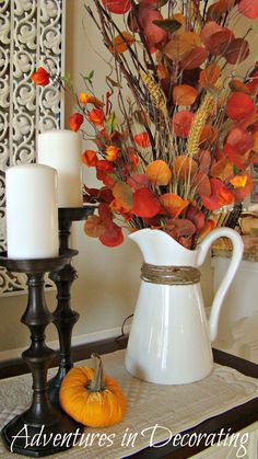 a white pitcher filled with flowers next to two candles