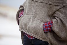 the back of a person wearing a sweater with a plaid shirt and jeans underneath it