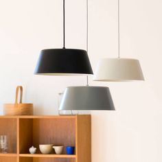 three lamps hanging from the ceiling above a table with bowls and cups on it in front of a bookcase