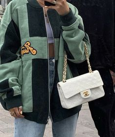 a woman standing on the street while looking at her cell phone and holding a white purse