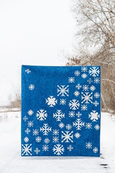 a blue blanket with white snowflakes on it sitting in the middle of a snowy field