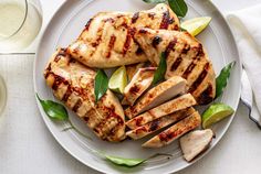 grilled chicken on a plate with garnishes and limes next to a glass of water